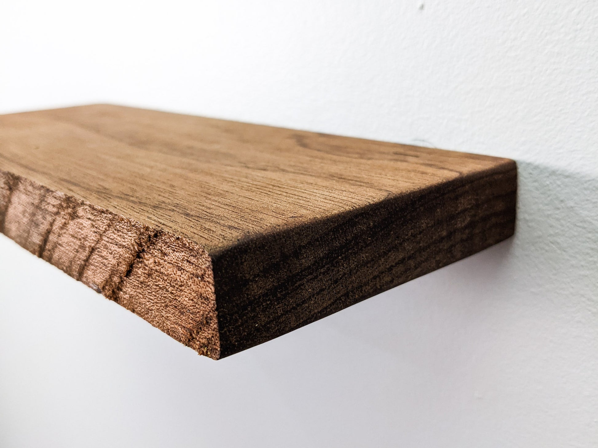 A side view of our mahogany medium wall-mounted live edge shelf. The live edge is textured and has not been sanded smooth to reveal the natural beauty of the mahogany wood. The top is bare.