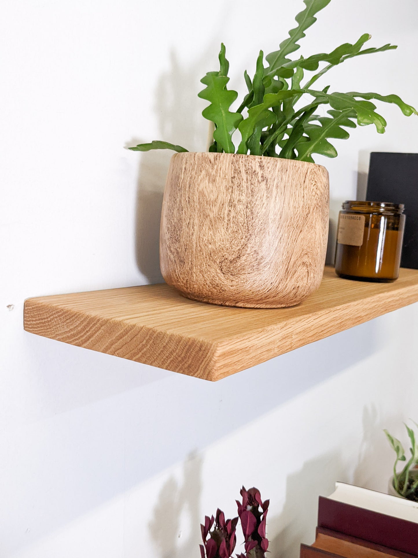 A close-up of the soft bevelled edges of a medium-duty oak floating shelves, a crispy fern sits on top with two vintage cndles beside it.