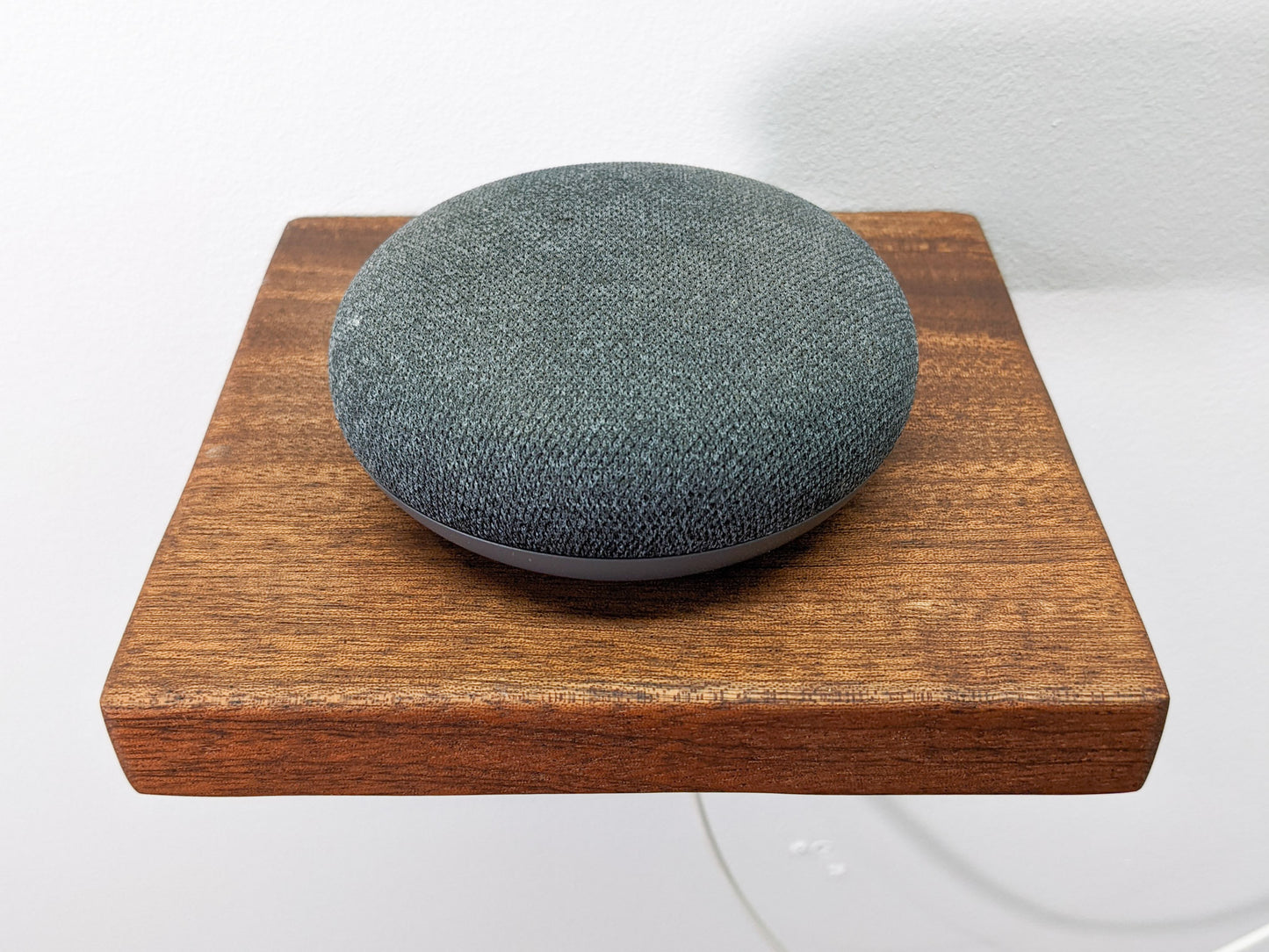 From above we see NookWoodworking's square mahogany floating shelf with hole for cable management. A round speaker sits on top and a white cord is threaded through a small, cleanly drilled hole in the back of the shelf.