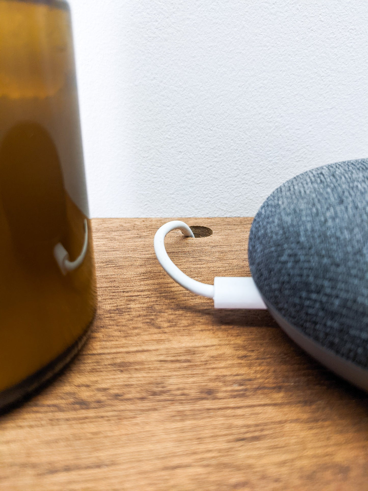 A close up view of a small hole that has been drilled in the back of our floating shelves to allow for seamless cord management. The speaker is half in the frame and sits to the right, a candle, more than half out of the frame, sits to the left. 