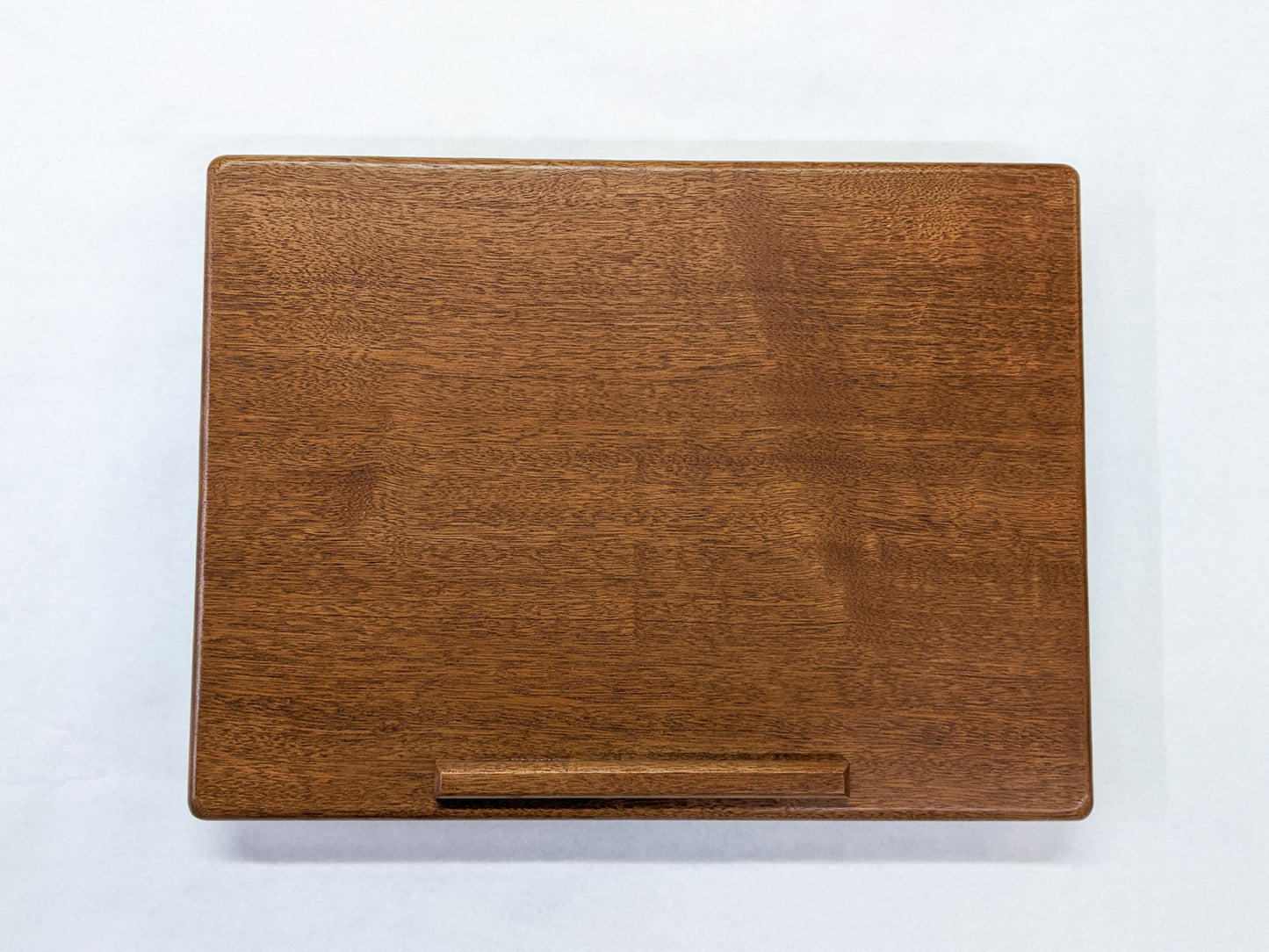 The surface of our Mahogany Leather Cushion Lap Desk. The mahogany wood is rich and the edges of the desk are soft and rounded. A protruding lip provides a stylish way to rest books or laptops. 